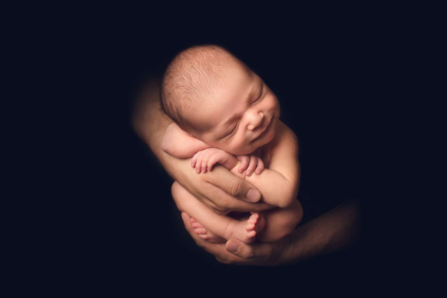 newborn photography with dad's hand - black back ground