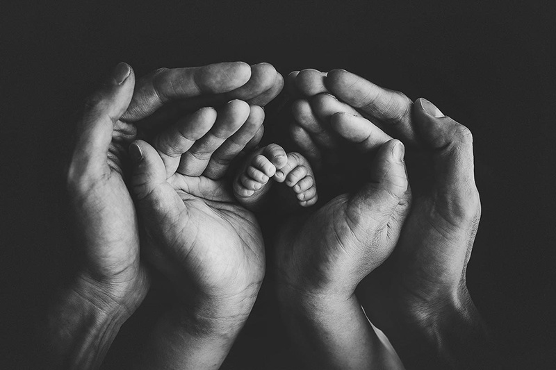 newborn photography with mom and dad hand in black and white