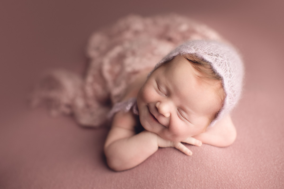 newborn baby girl smiles - hat - pink background