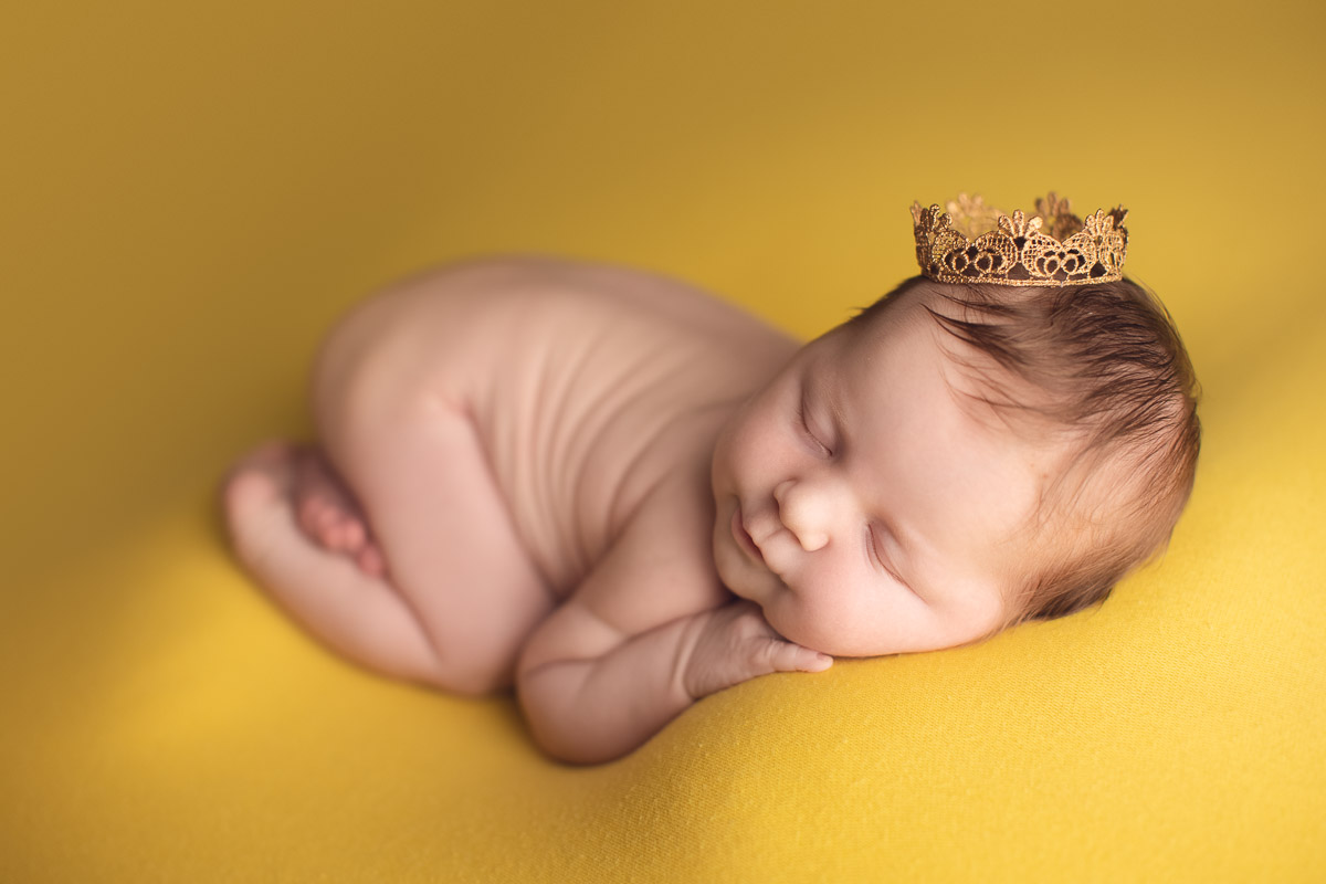 newborn baby girl smiles in yellow background - crown
