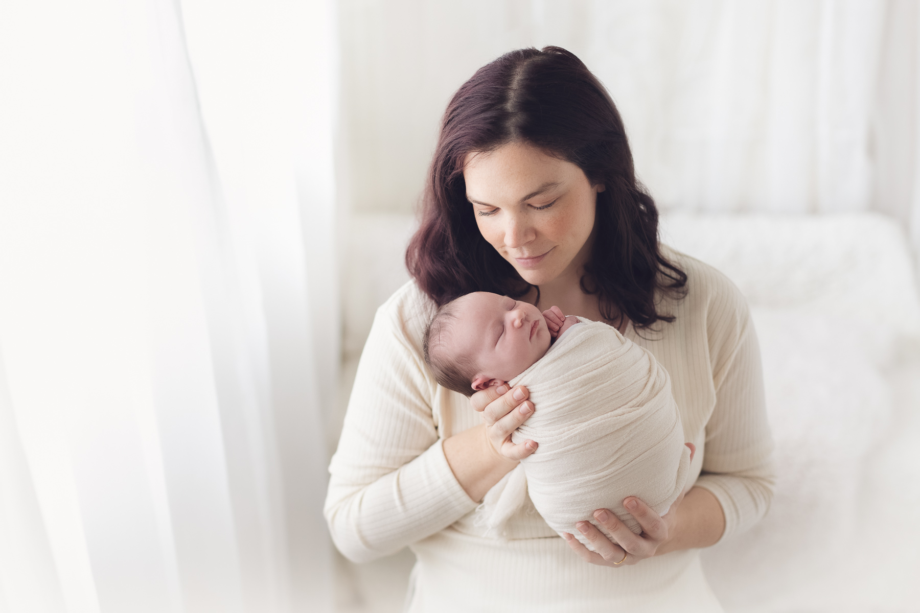 best newborn photographer in surrey - mom holding newborn baby in white background and natural light