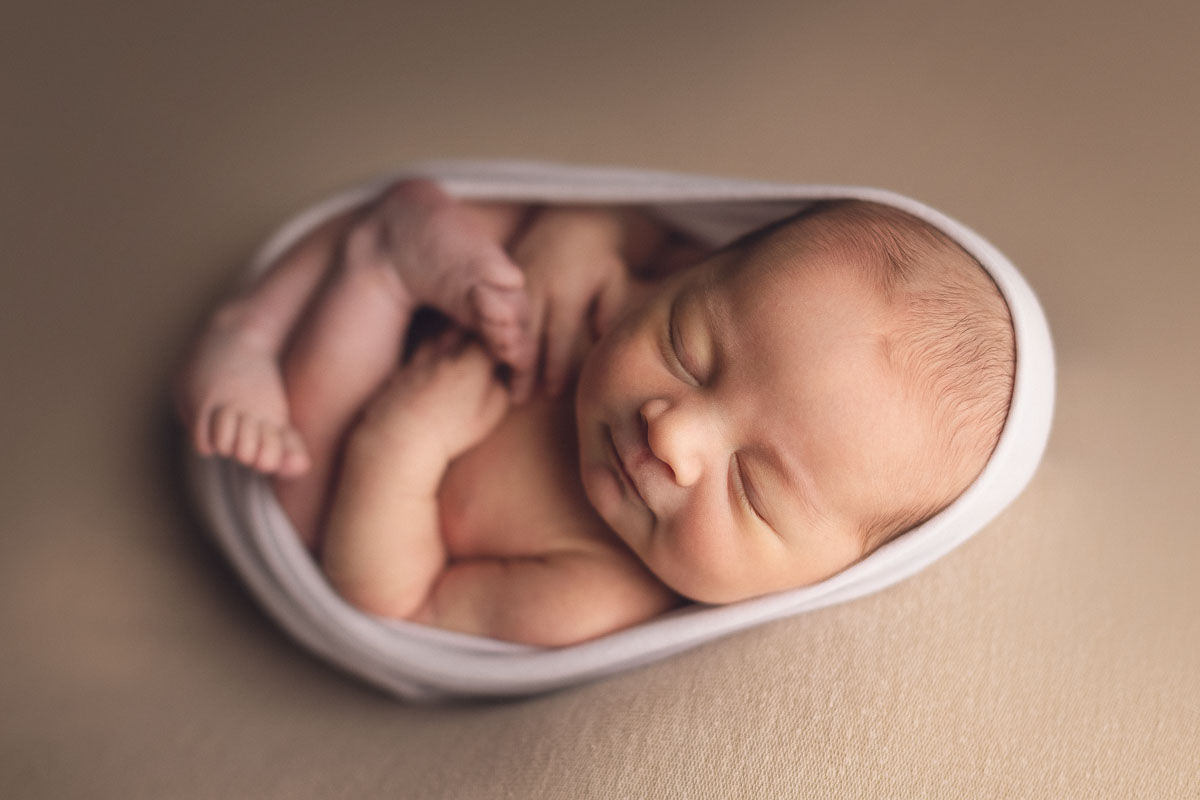 3 days old newborn baby girl on a cream background smiling - white wrap